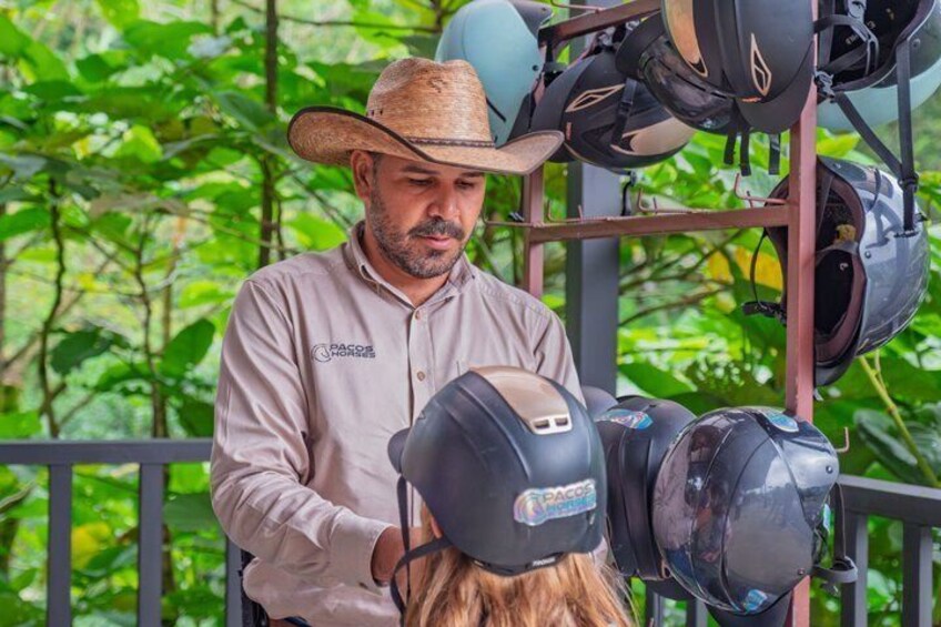 A person wearing a cowboy hat and a light-colored shirt standing next to a helmet rack with helmets. 3
