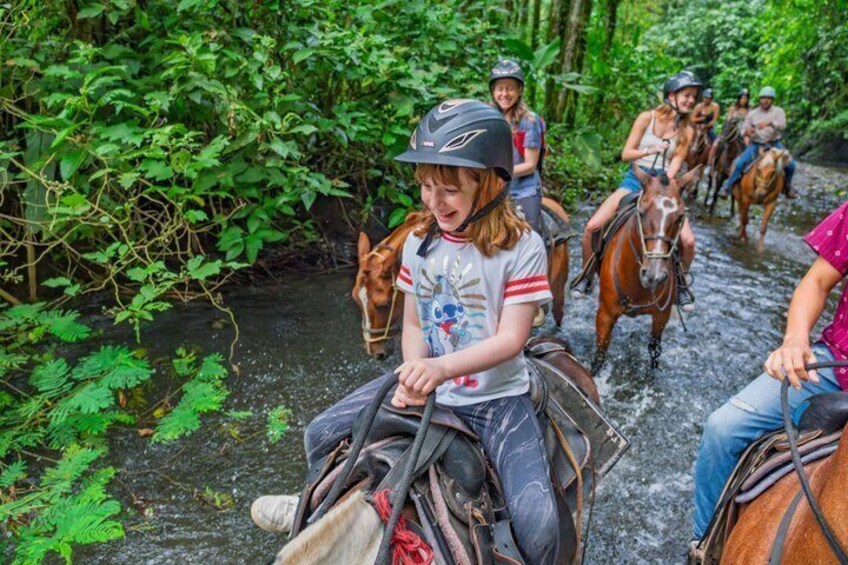 People riding horses along a narrow waterway surrounded by dense greenery. 1