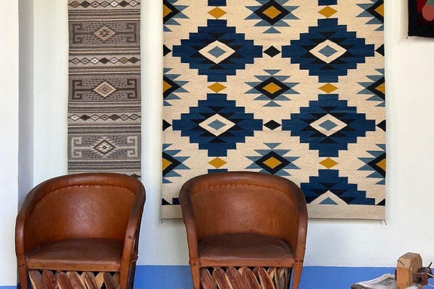Two wooden chairs in front of a wall with two patterned rugs. 2