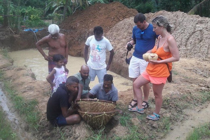 A group of people near a muddy water body, some standing and some sitting, with a large basket in the foreground. 3