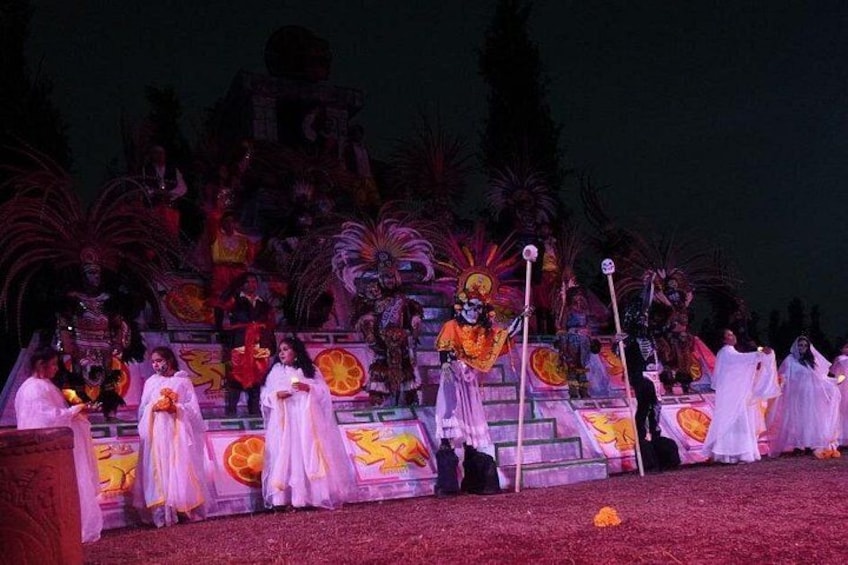 Un palco con artisti in costumi bianchi, uno sfondo con decorazioni colorate e una scalinata che conduce a una piattaforma. 1