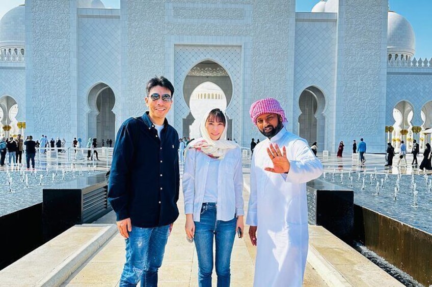 Trois personnes se tiennent devant un bâtiment blanc, orné d’arches et agrémenté d’une fontaine. 1