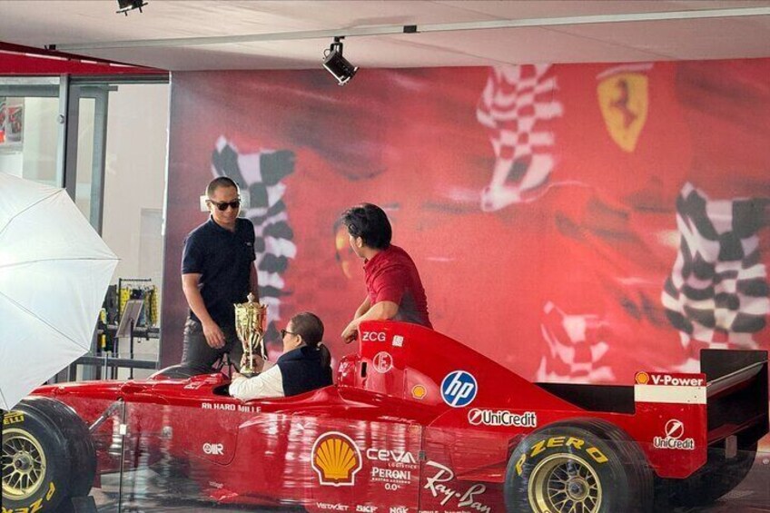 Une voiture de course rouge, ornée de divers logos, dont ceux de Shell et HP, est garée à l’intérieur. 2