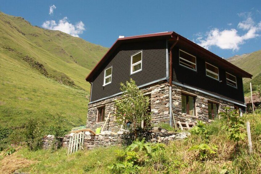 A stone house with a dark roof, surrounded by lush green hills. 4