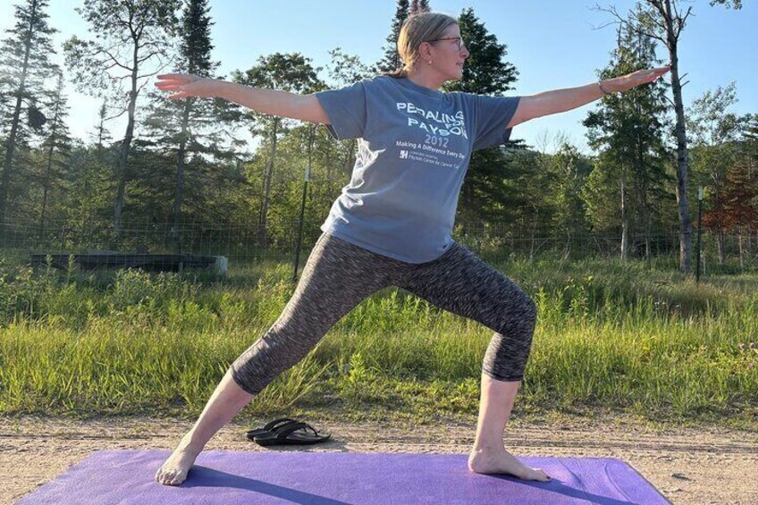 En person laver en yogastilling på en lilla måtte udendørs. 1