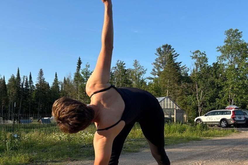 En person udfører en yogastilling udendørs med træer og en bygning i baggrunden. 5