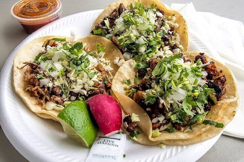 Tre tacos med strimlat kött, tärnade lökar och koriander, serverade på en vit tallrik. 4