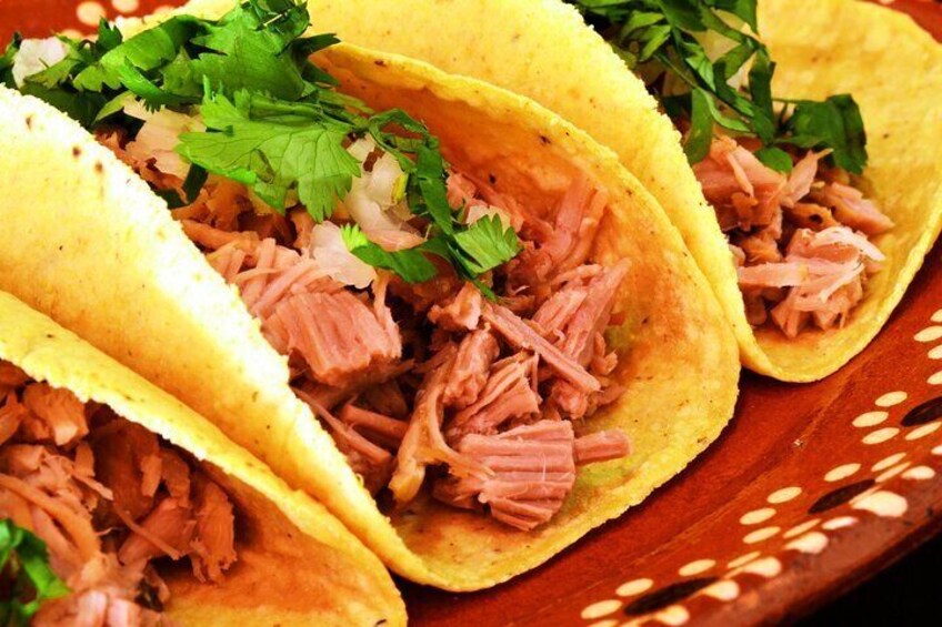 Tre tacos med strimlat kött och koriander, serverade på en träbricka. 1