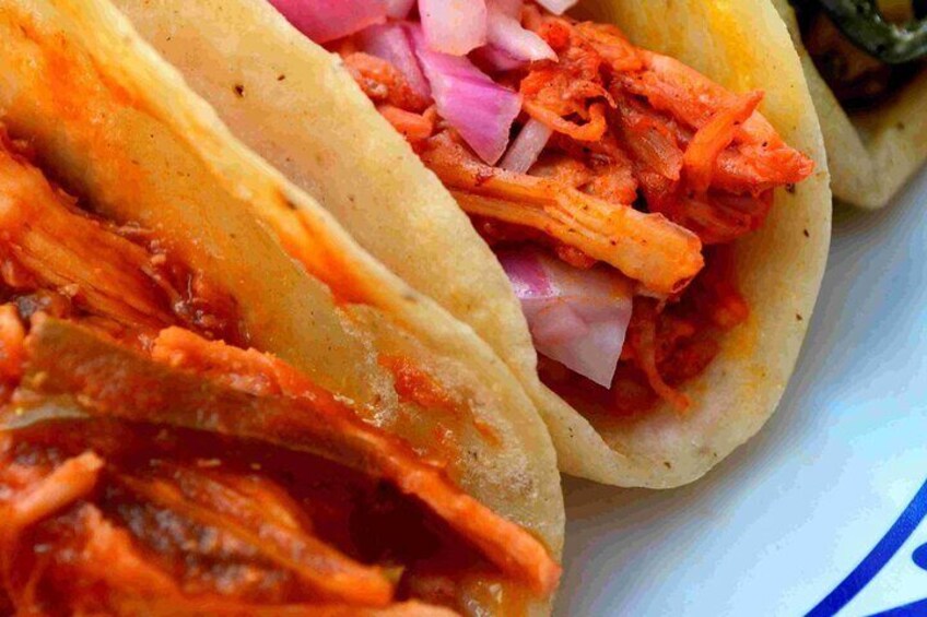 En tallrik med tre tacos fyllda med strimlat kött, rödlök och en röd sås. 2