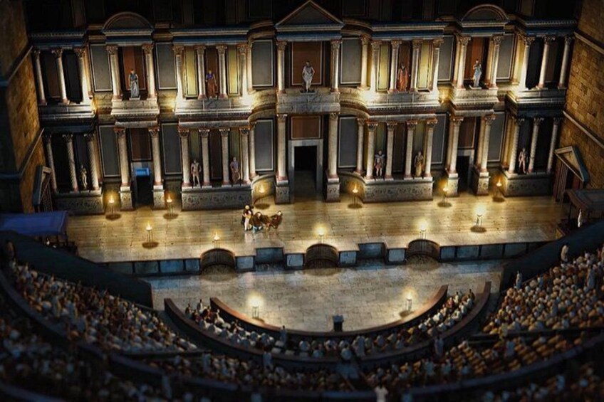 Een overdekt amfitheater met een centraal podium, terrasvormige zitplaatsen en klassieke architectuur. 4