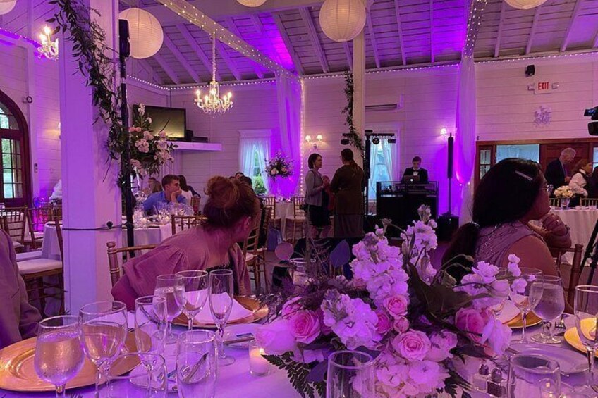 Ein Festsaal mit gedeckten Tischen für eine festliche Veranstaltung, dekoriert mit Blumen und beleuchtet durch dezentes Licht. 2
