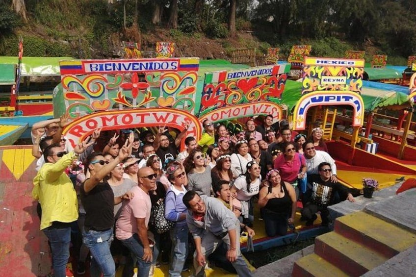 A group of people posing in front of a colorful amusement park ride with a sign that reads 'BIENVENIDOS' and 'PROMOTWIS'. 3