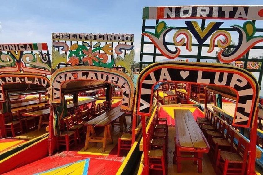A colorful outdoor seating area with multiple tables and chairs, surrounded by vibrant signage. 1