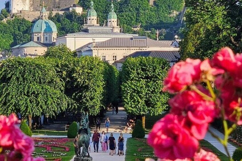 A park with a large building with domed roofs, people walking, and a statue in the foreground. 5