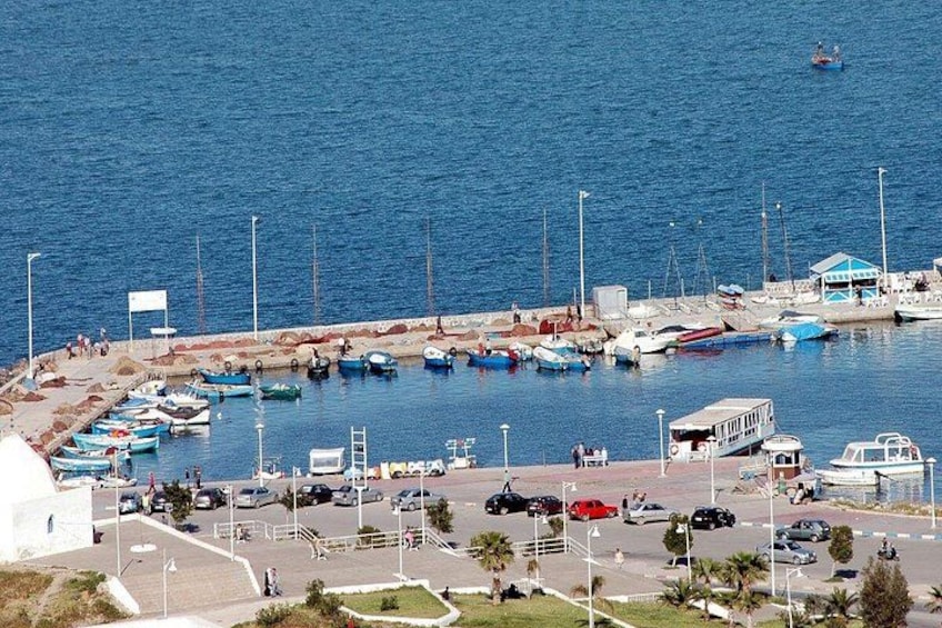 A coastal marina with boats docked, a small boat in the water, and a road with vehicles. 2