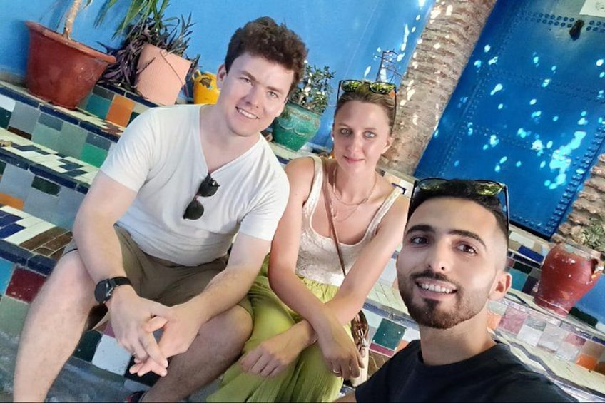 Three people sitting by a pool with potted plants and a blue tiled wall in the background. 3