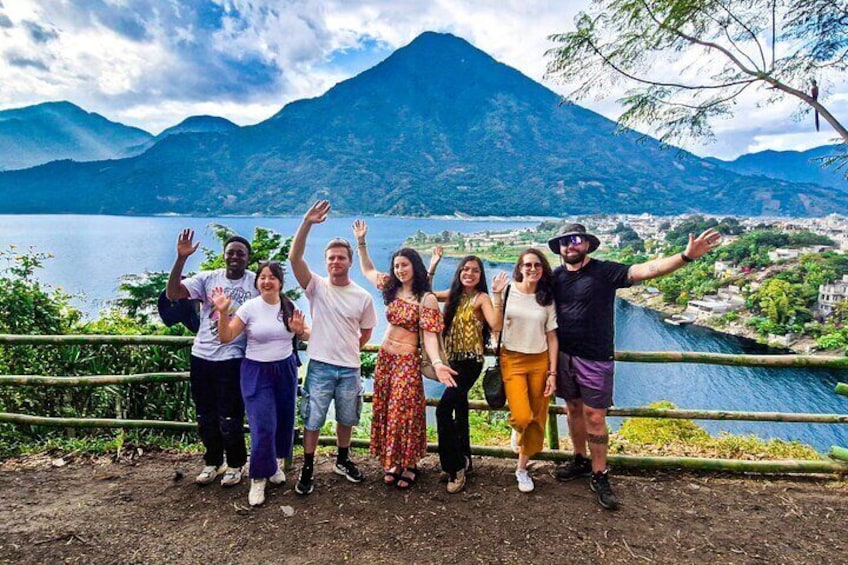 Un groupe de personnes se tient sur un chemin de terre, avec un lac et des montagnes en arrière-plan. 1