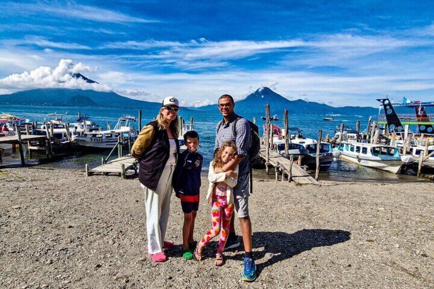 Une famille se trouve sur un quai, avec des bateaux et une montagne en arrière-plan. 5