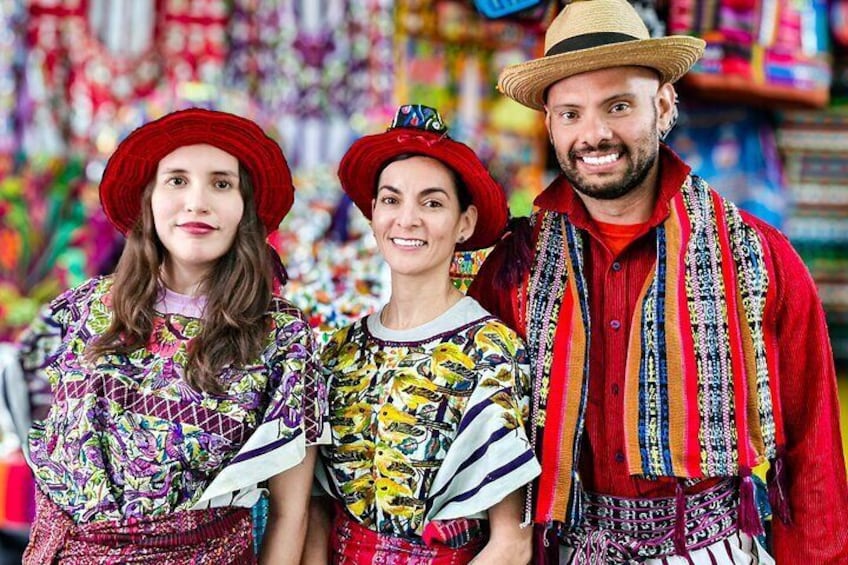 Trois personnes, vêtues de costumes traditionnels aux couleurs vives, se trouvent sur un marché. 3