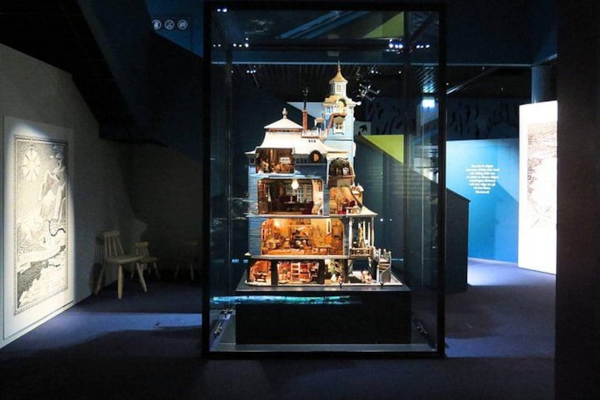 Een glazen displaykast met een meerlaagse constructie, mogelijk een model of tentoonstelling, in een schemerige ruimte met een kaart en een stoel op de achtergrond. 4