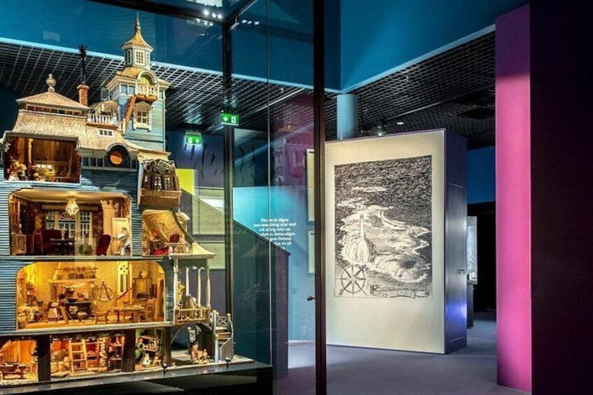 Een museumexpositie met een gedetailleerd model van een gebouw en een groot kunstwerk in een lijst. 1