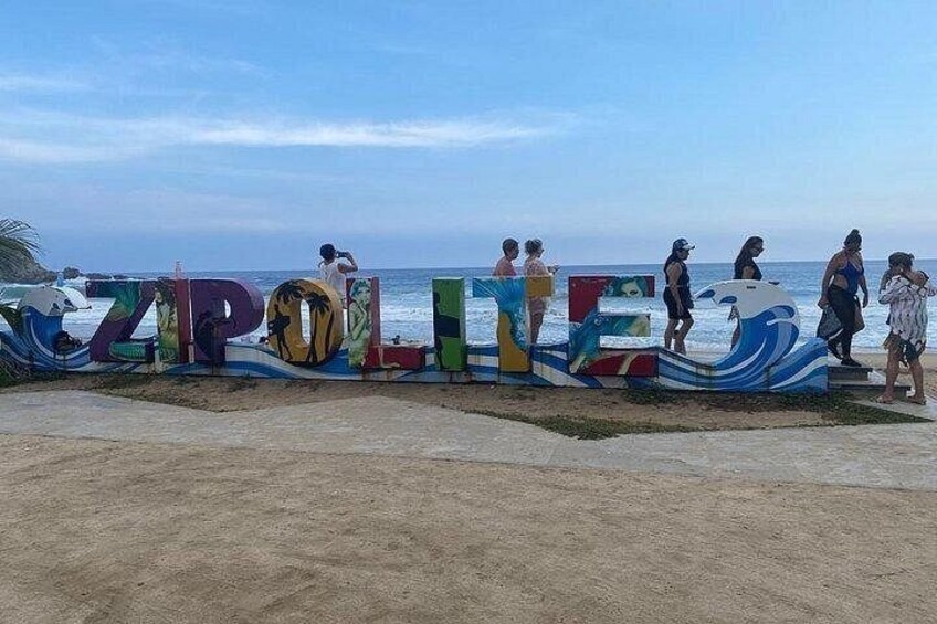 A beach with colorful letters spelling 'ZIPOLI' and people walking along the shore. 2