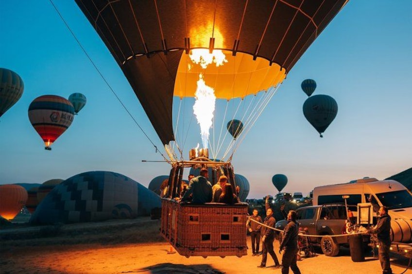 A hot air balloon with flames, surrounded by other balloons and ground crew. 4