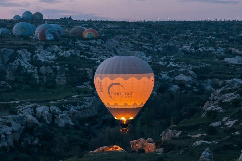 A hot air balloon with 'TURQUA' written on it, flying over a rocky landscape with other balloons in the background. 5