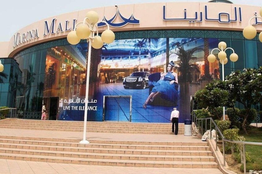 The Marina Mall entrance with a large advertisement, steps leading up to the entrance, and decorative street lamps. 4