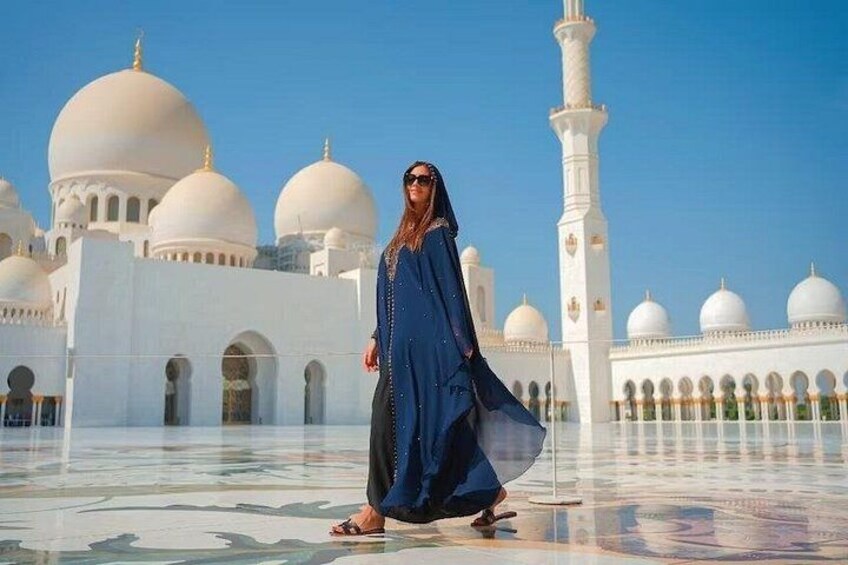 A person in a blue dress walking in front of a white building with domes and minarets. 5
