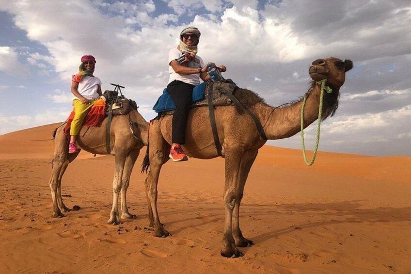 Deux personnes montent des chameaux dans un désert, avec des dunes de sable en arrière-plan. 4
