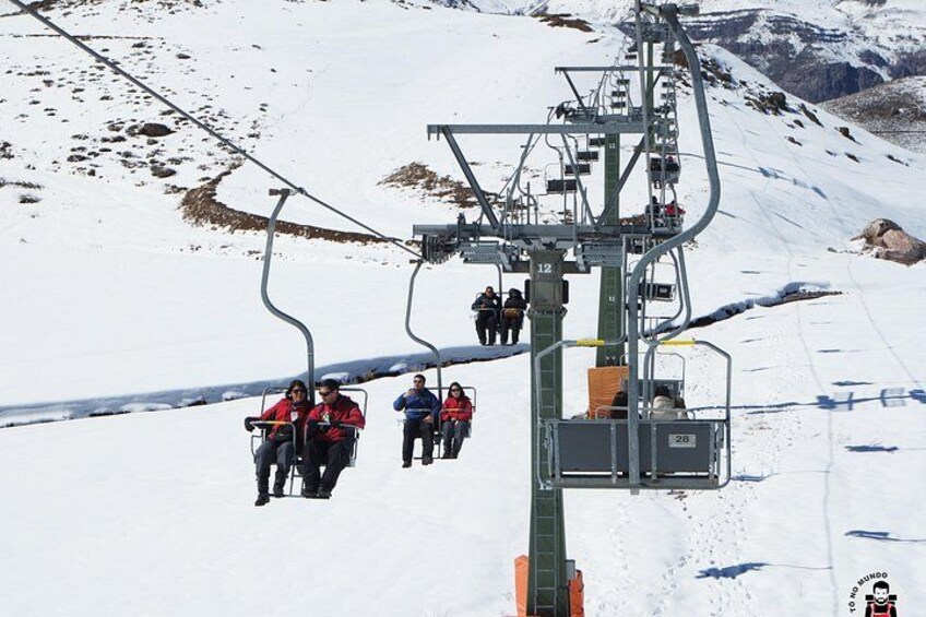 Eine Seilbahn mit Skifahrern in roten Jacken, die einen verschneiten Hang hinauffährt. 2