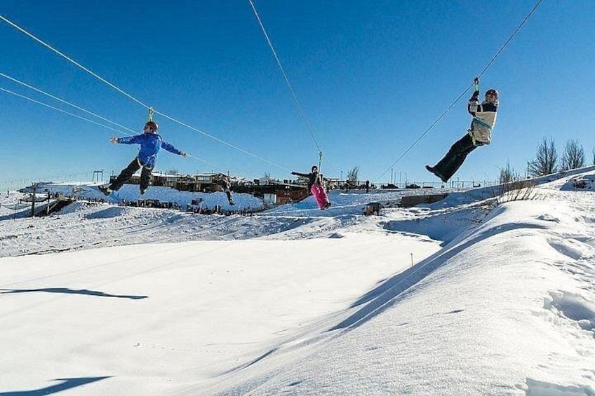 Schneebedeckte Landschaft mit Skipiste und einer Person in einer blauen Jacke, die auf einem Skilift einen Trick vollführt. 1