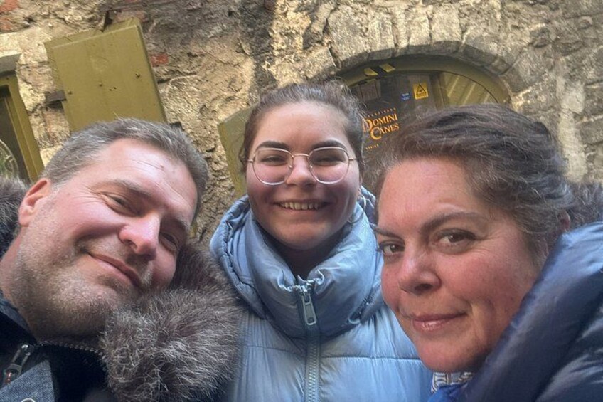 Drei Personen vor einem Steinhaus mit einer Tür, auf der 'DOMINI GINE' steht. 3