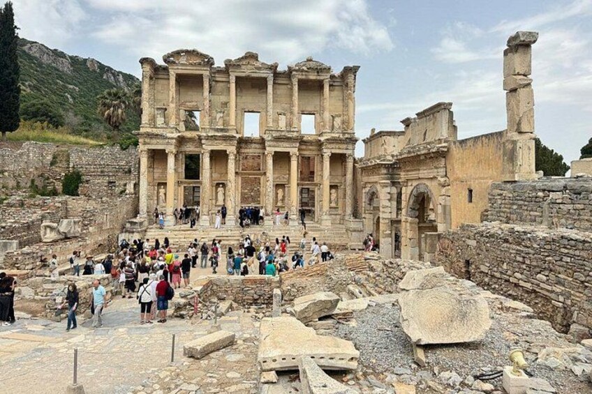 The ancient ruins of a large, multi-story structure with columns and arches, surrounded by a crowd of tourists. 5