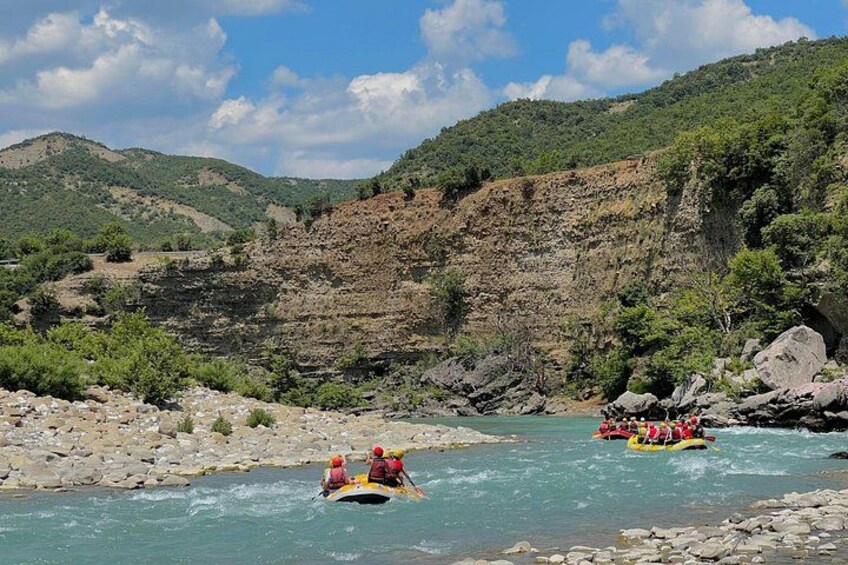A river with people rafting, surrounded by rocky cliffs and greenery. 4