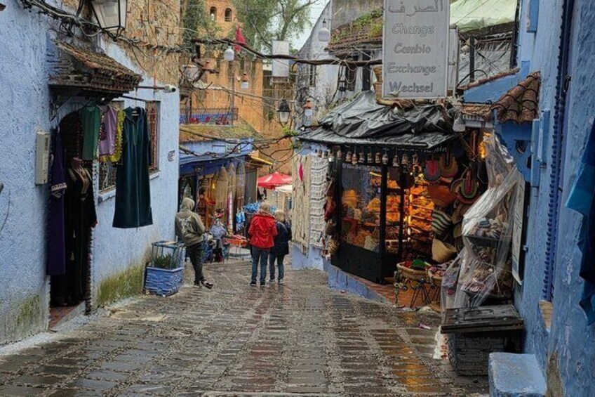 Una calle estrecha con tiendas, un letrero y una persona caminando. 3