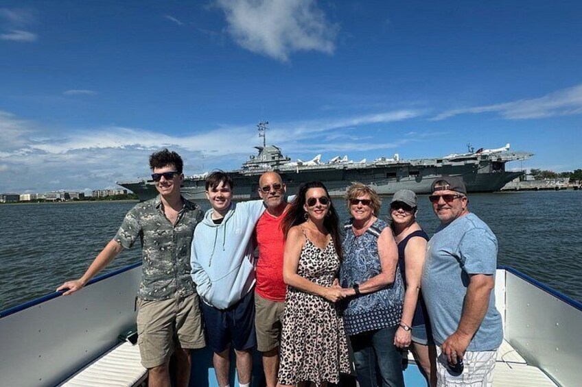 A group of people on a boat with an aircraft carrier in the background. 2