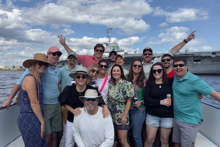 A group of people on a boat with an aircraft carrier in the background. 4