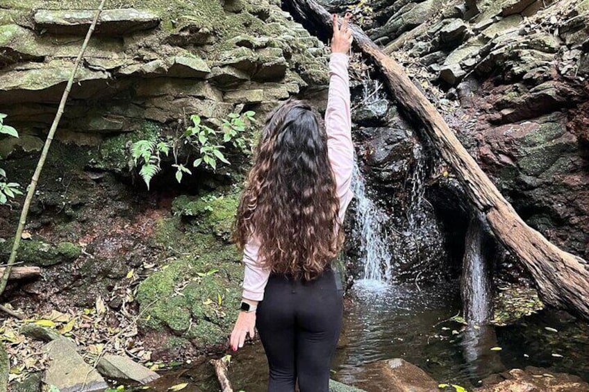 A person reaching towards a waterfall in a rocky area. 5