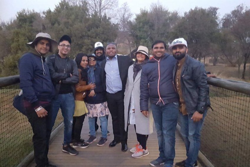 Un gruppo di persone in piedi su un ponte di legno, con una recinzione su entrambi i lati, circondato da alberi. 2