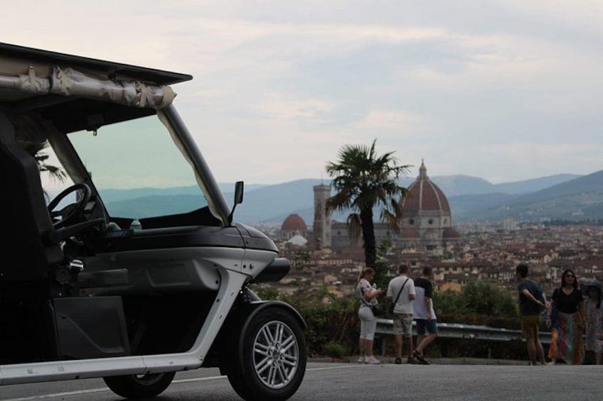 Un coche descapotable estacionado en una carretera, con un paisaje urbano y montañas al fondo. 1