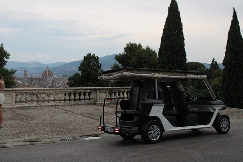 Un carrito de golf estacionado en un área pavimentada, con un paisaje urbano y montañas al fondo. 4