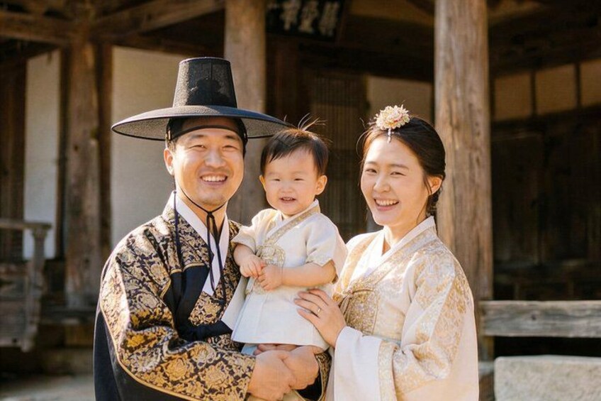 A person in traditional attire holding a child, standing in front of a wooden structure with columns. 3