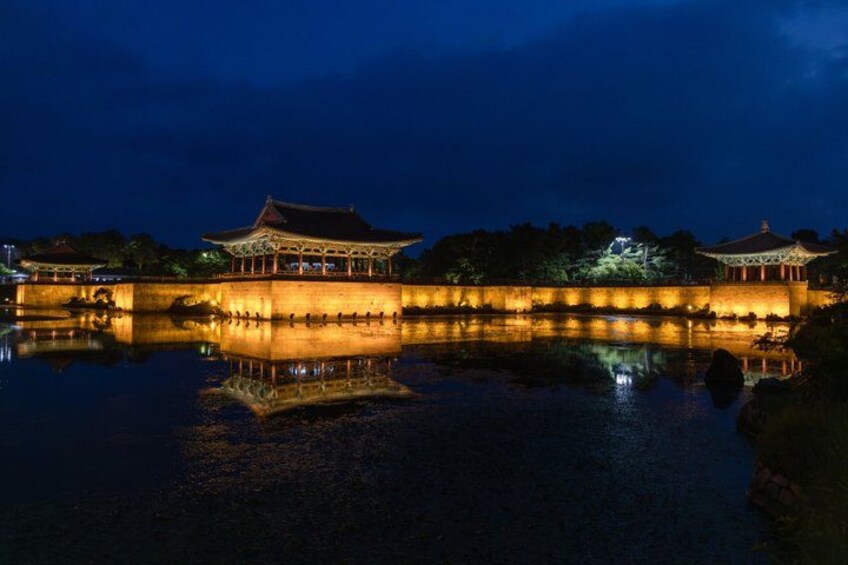 A traditional Chinese pavilion illuminated at night, reflecting on a calm water surface. 4