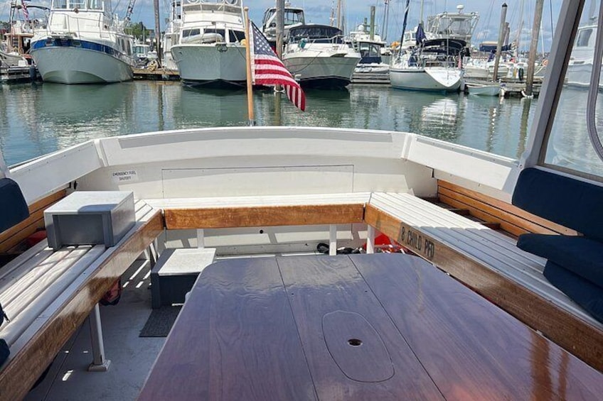 A boat deck with a wooden table, cushioned seating, and an American flag. 5