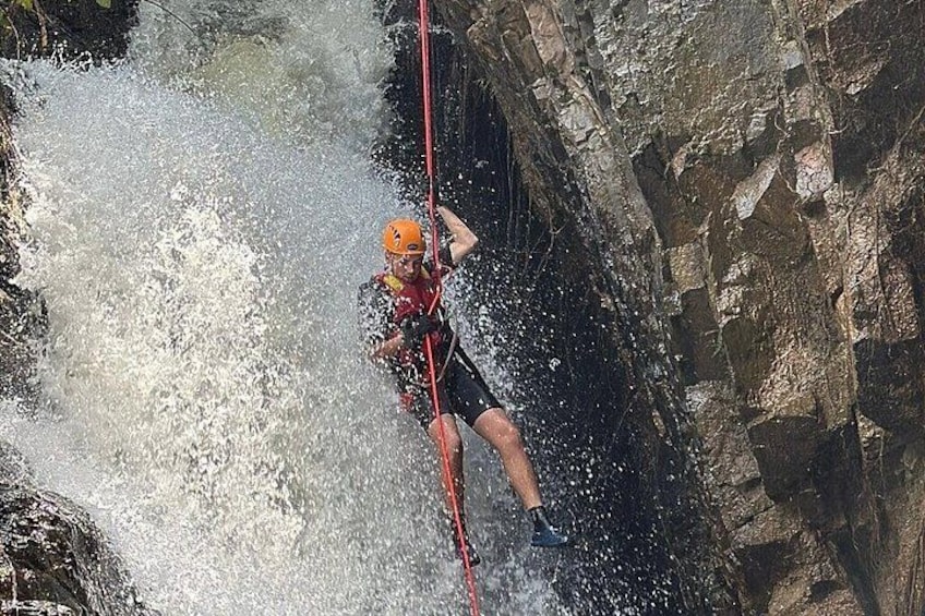 A person rappelling down a rocky cliff with water splashing around. 3