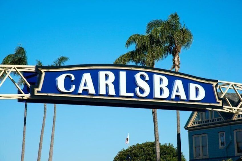 Un panneau bleu avec le mot «
CARLSBAD
» écrit en lettres blanches, des palmiers et un bâtiment en arrière-plan. 3