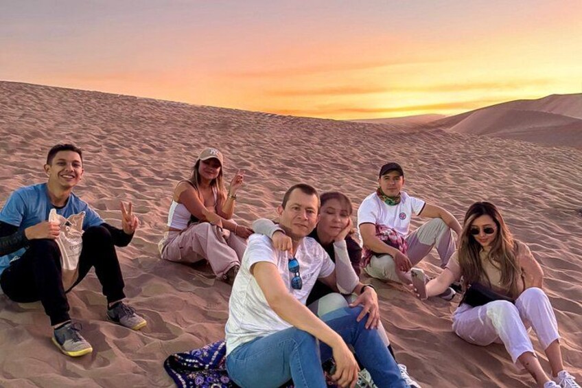 A group of people sitting on sand dunes during sunset. 2