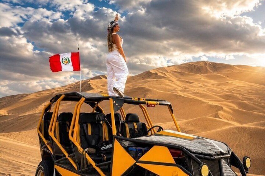 Una persona está sobre una duna con una bandera, un buggy todoterreno y un paisaje desértico. 1